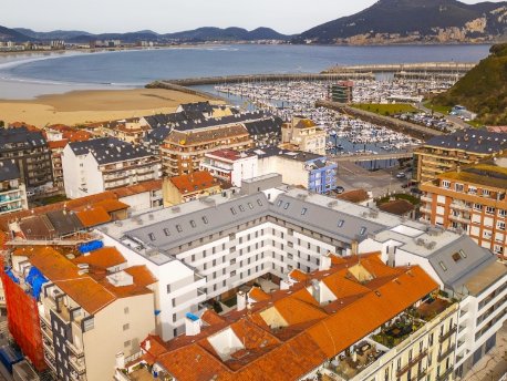 En el centro, la promoción Noray de Neinor Homes, comercializada bajo la marca AEDAS Homes, en Laredo (Cantabria) con el mar al fondo