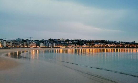 Una vista de una ciudad costera española con edificios residenciales iluminados y una playa vacía, ilustrando el potencial para invertir en vivienda en la costa española como apuesta segura.