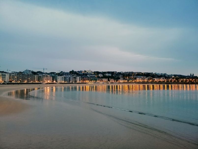 Una vista de una ciudad costera española con edificios residenciales iluminados y una playa vacía, ilustrando el potencial para invertir en vivienda en la costa española como apuesta segura.