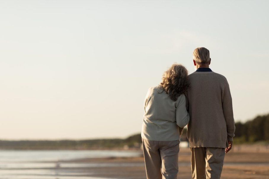 Pareja de jubilados paseando de la mano por la playa al atardecer en la costa española.