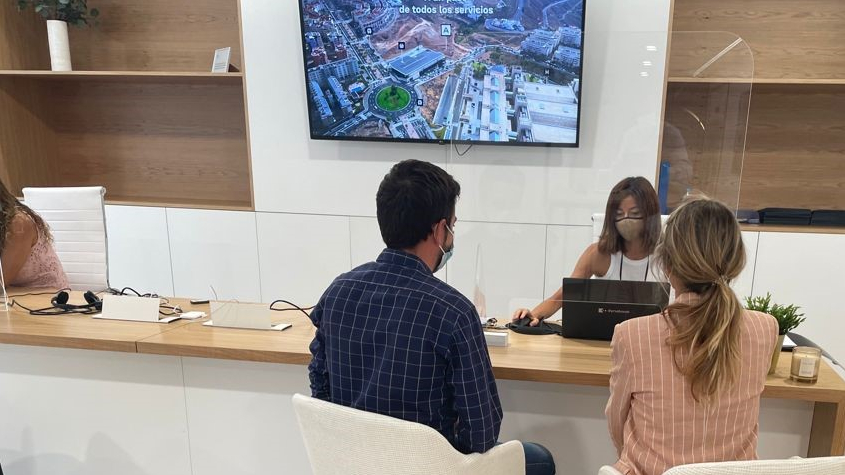 Una comercial atiende a una pareja de jóvenes interesados en Gazmira en la oficina de AEDAS Homes en Las Palmas de Gran Canaria.